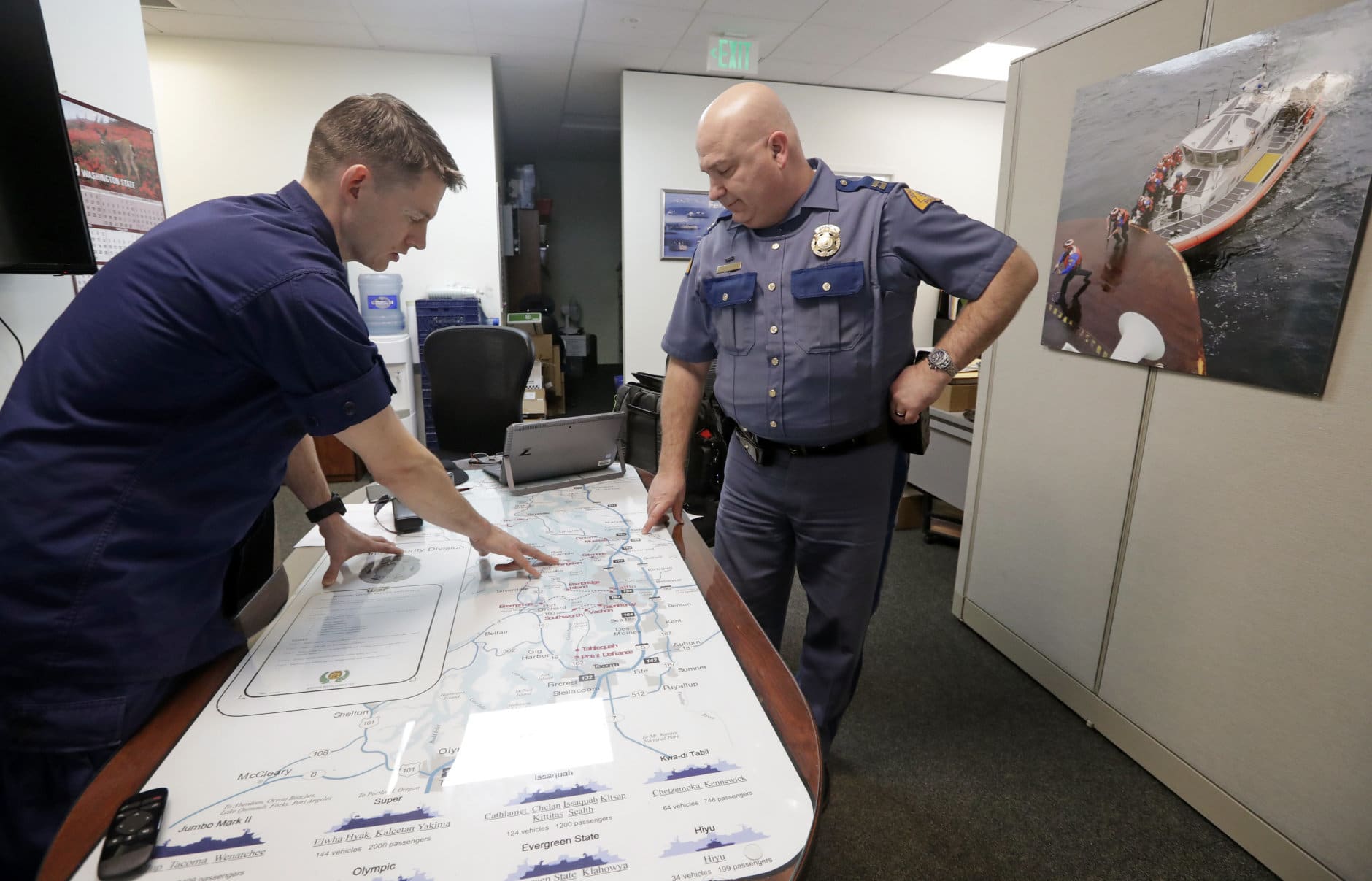 U.S. Coast Guard Lt. Cmdr. Blair Sweigert, left, who missed a paycheck a day earlier during the partial government shutdown, works with Washington State Patrol Capt. Dan Atchison in a shared office where they coordinate marine security at Sector Puget Sound base Wednesday, Jan. 16, 2019, in Seattle. The Coast Guard is part of the U.S. Department of Homeland Security, which is unfunded during the shutdown, now in its fourth week. (AP Photo/Elaine Thompson)